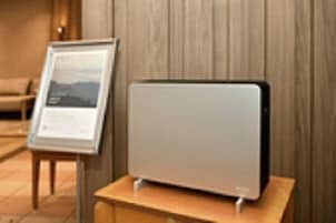 Una stanza moderna con parete rivestita in legno, un cartello informativo incorniciato e un dispositivo elettronico elegante e minimalista su un tavolo in legno.