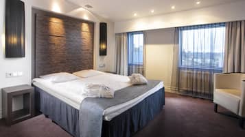 Ein modernes Hotelzimmer mit einem großen Bett, Blick auf die Stadt durch das Fenster und einer Sitzecke.