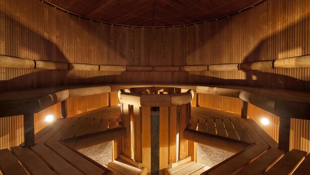 A sauna with wooden benches arranged in a semi-circular pattern, a central pillar, and a wooden ceiling. - Tallink Hotel Riga  (Riga)