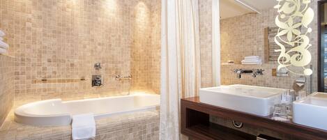 A modern bathroom with a large bathtub, two sinks, and a mirror with a decorative frame.