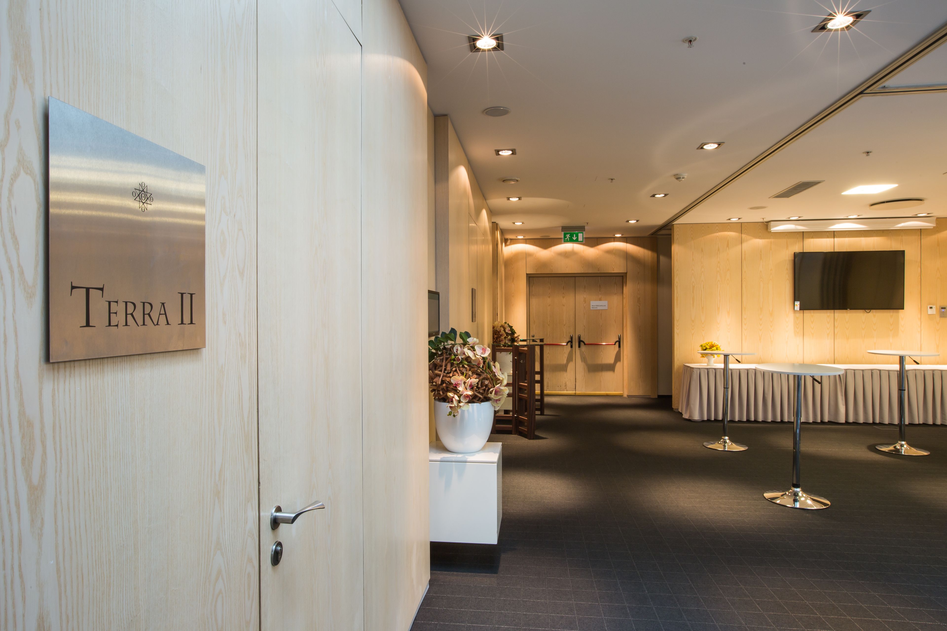 Eine Hotelhalle mit einer Rezeption, einem Schild mit der Aufschrift "Terra II" und einer Sitzecke mit Tischen und Stühlen.