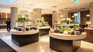 A modern hotel lobby with three buffet stations, each with a variety of food items and decorative plants. - Tallink Hotel Riga  (Riga)