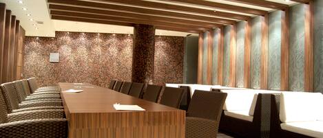 Un salón de conferencias con una larga mesa de madera, sillas acolchadas y paredes con diseño.