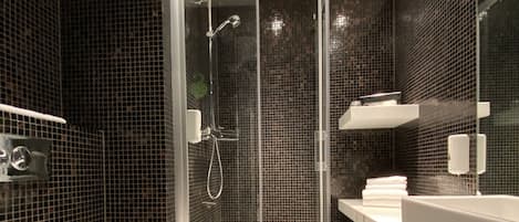 Un baño moderno con ducha envuelta en vidrio, inodoro blanco y un espejo grande sobre el lavamanos.