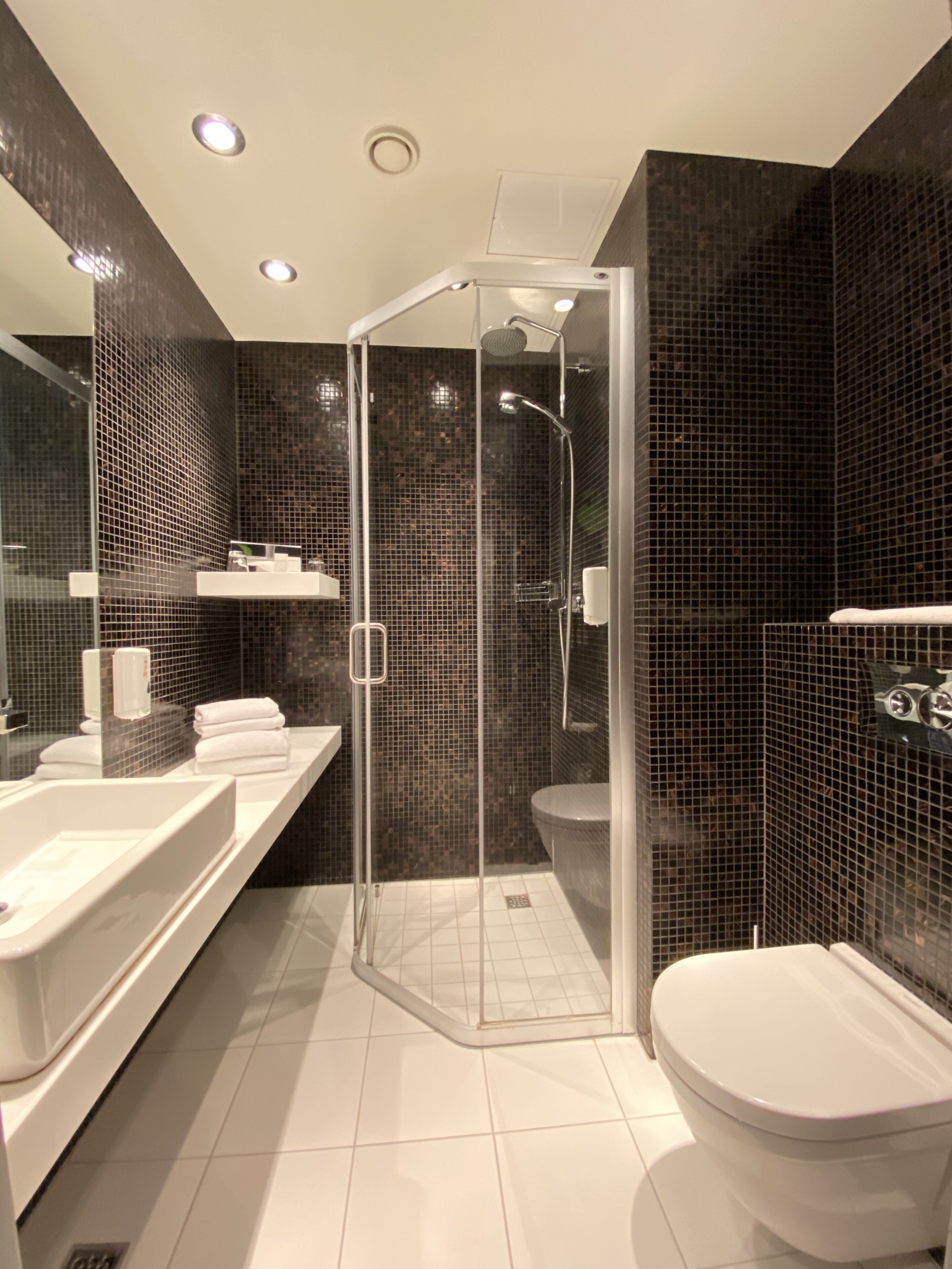 Un bagno moderno con doccia vetro, lavandino bianco e water.