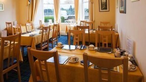 A dining area with multiple tables and chairs, large windows with curtains, and framed pictures on the walls. - Heriott Park Guest House (Edinburgh)