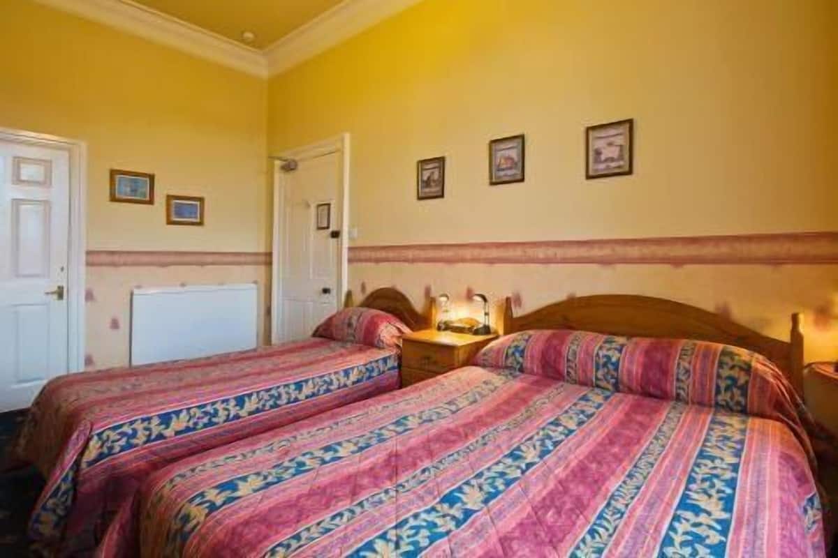 Quarto com duas camas, uma porta branca e parede com quadros.