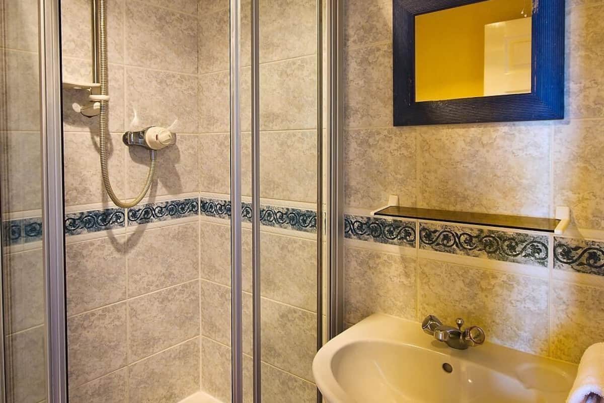 Uma casa de banho com chuveiro envidraçado, lavatório com espelho em cima e detalhes em azulejos decorativos.