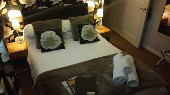 Una cama bien hecha con almohadillas florales, una toalla doblada y una revista sobre la cama.