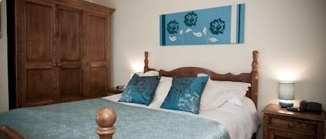 Un dormitorio con un armario grande de madera, una cama con colcha azul y blanca, y un cuadro colgado en la pared.