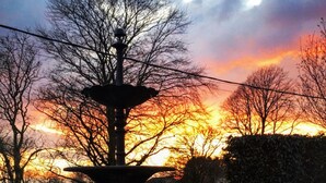 A fountain with swan sculptures in a circular basin, surrounded by grass and trees, with a sunset in the background. - Plas Hyfryd Hotel (Narberth)