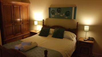 A bedroom with a large wooden wardrobe, a bed with green and white bedding, two bedside lamps, and a painting above the bed.