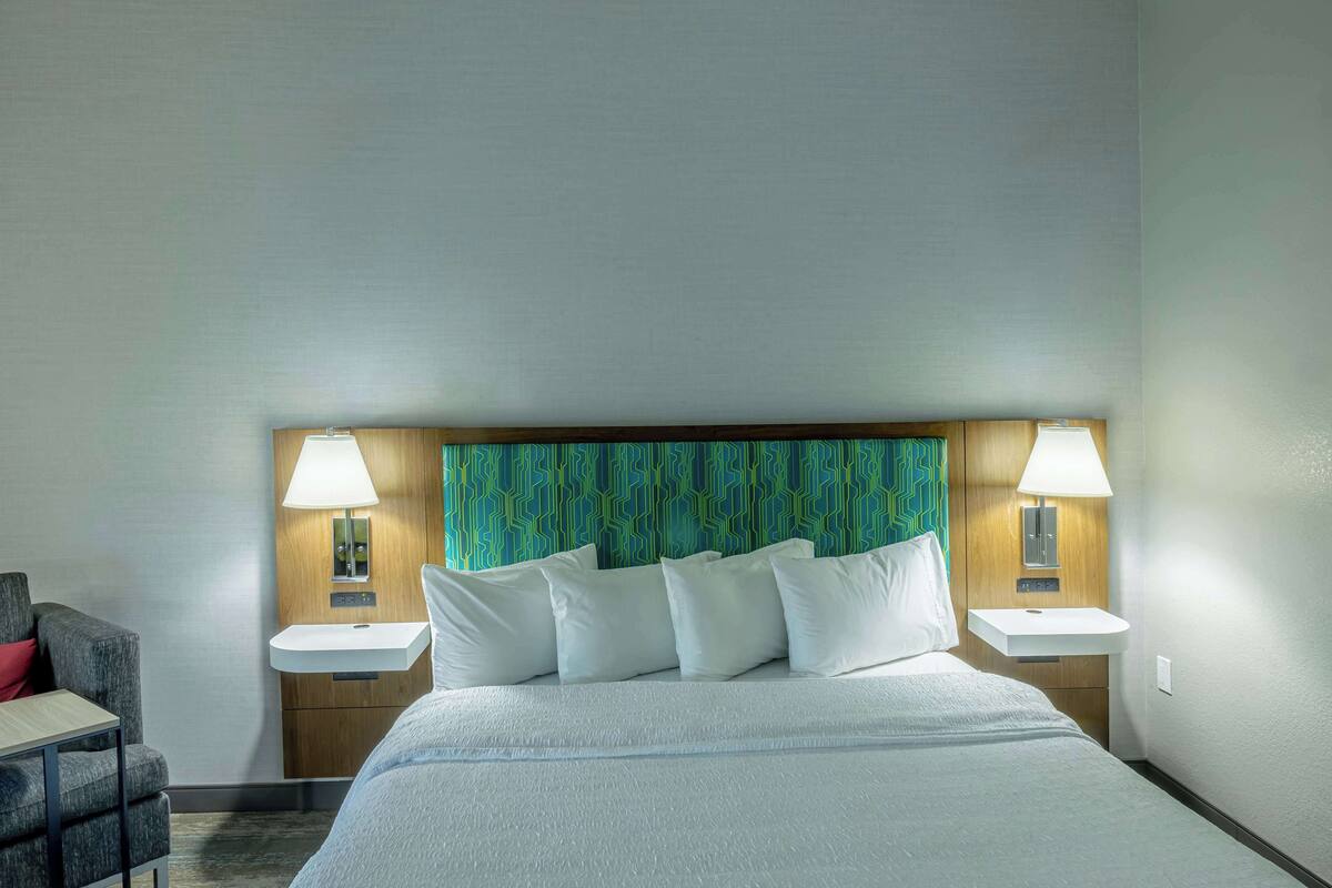 A hotel room with a large bed, two bedside tables, a nightstand, a desk, and a chair.