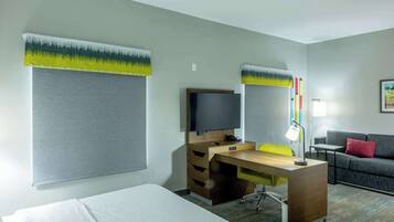 Una habitación de hotel con cama, escritorio con computadora, una silla, sofá y televisión.