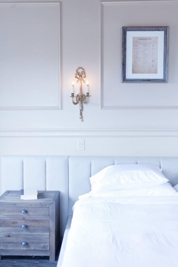 Un dormitorio ordenado con cama, mesita de noche, lámpara de pared y un menú enmarcado en la pared.