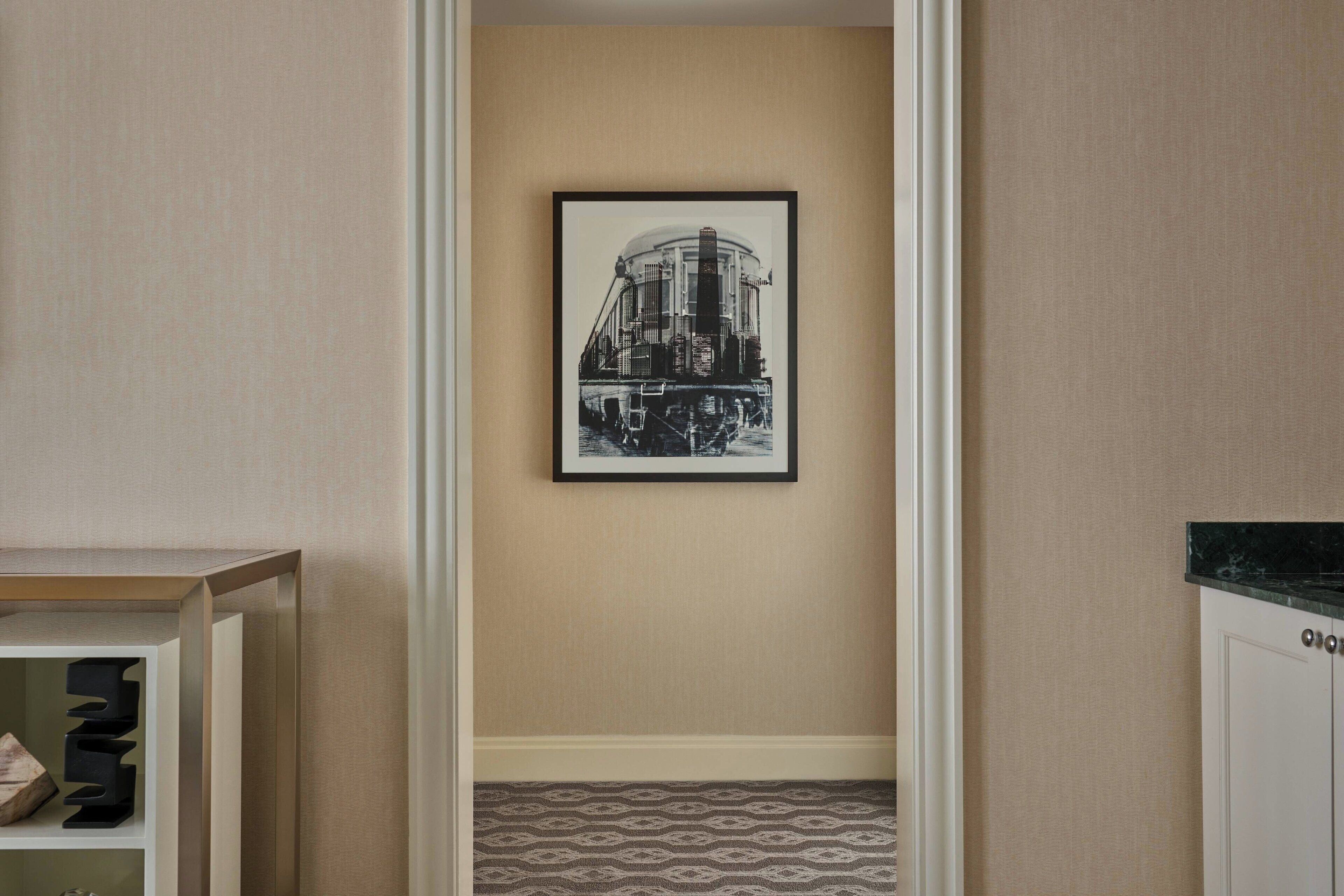 A hallway with a framed black and white photograph on the wall, patterned carpet, and a wooden cabinet with a marble countertop.