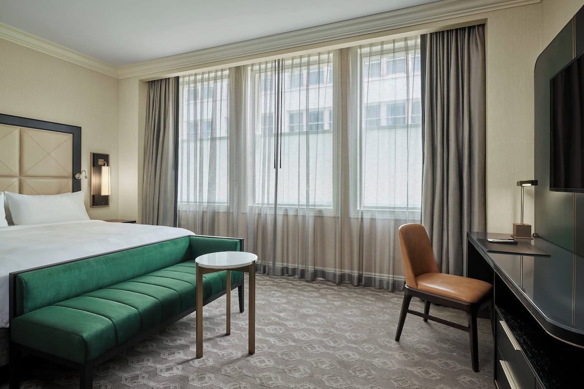 Une chambre d’hôtel avec un grand lit, un canapé vert, une petite table, un fauteuil en cuir et un téléviseur posé sur un meuble.