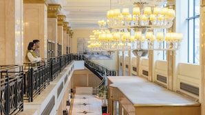 Un ampli vestíbul d'hotel amb un sostre alt, un gran candelabrum i una escala que condueix a un pis superior.