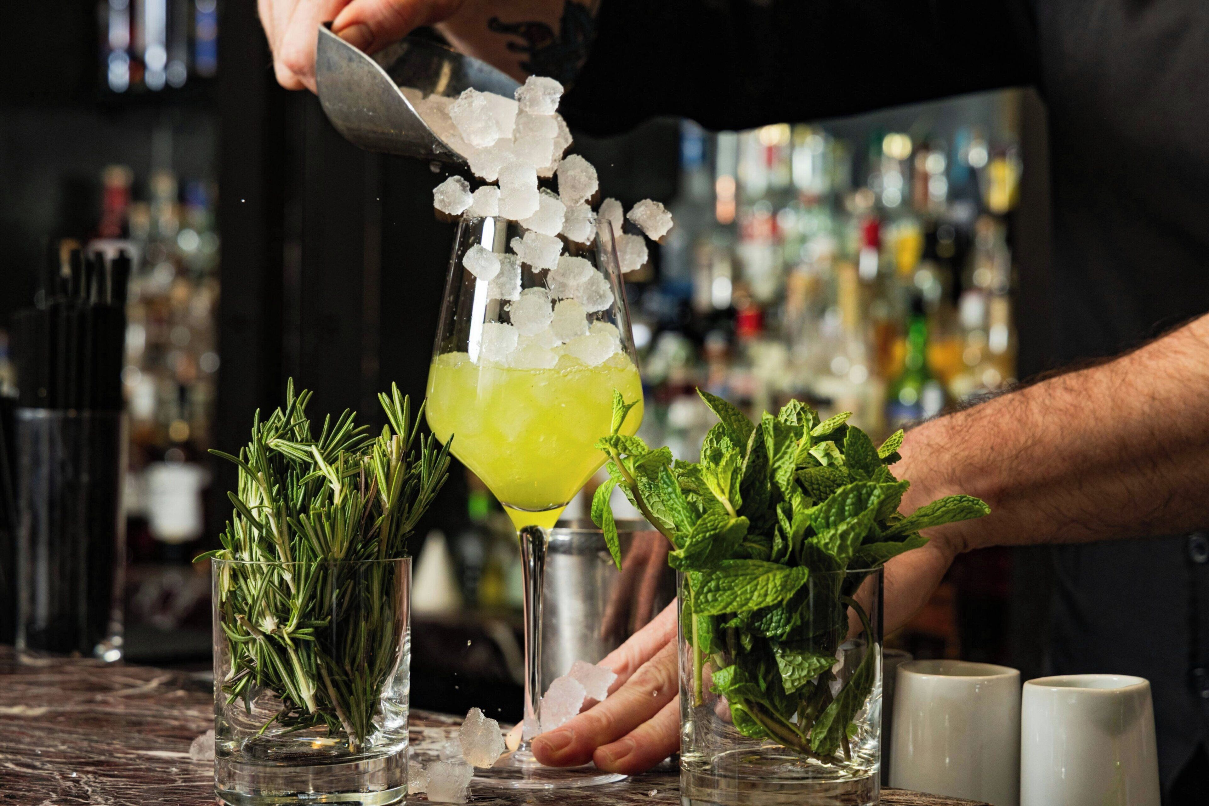 Een bartender bereidt een drankje toe met ijs en kruiden.