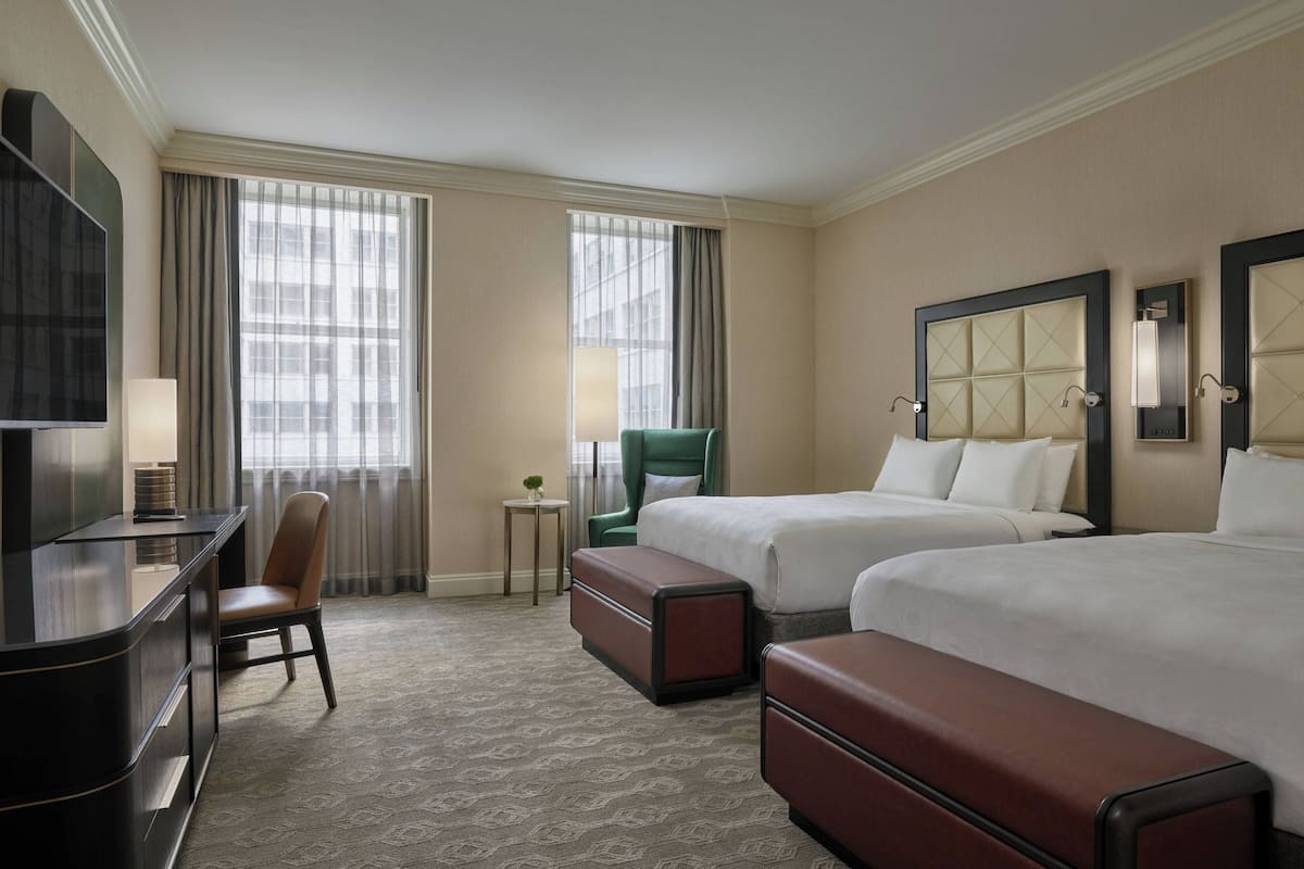 Une chambre d’hôtel avec deux lits, un bureau, une chaise et un téléviseur.