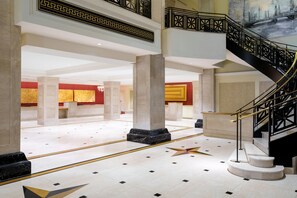 A spacious lobby with a grand staircase, marble columns, and a star-shaped floor design.