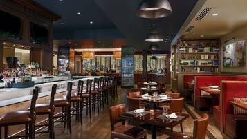 Uma área de bar com diversas opções de assento, incluindo banquetas e mesas, e uma adega ao fundo.