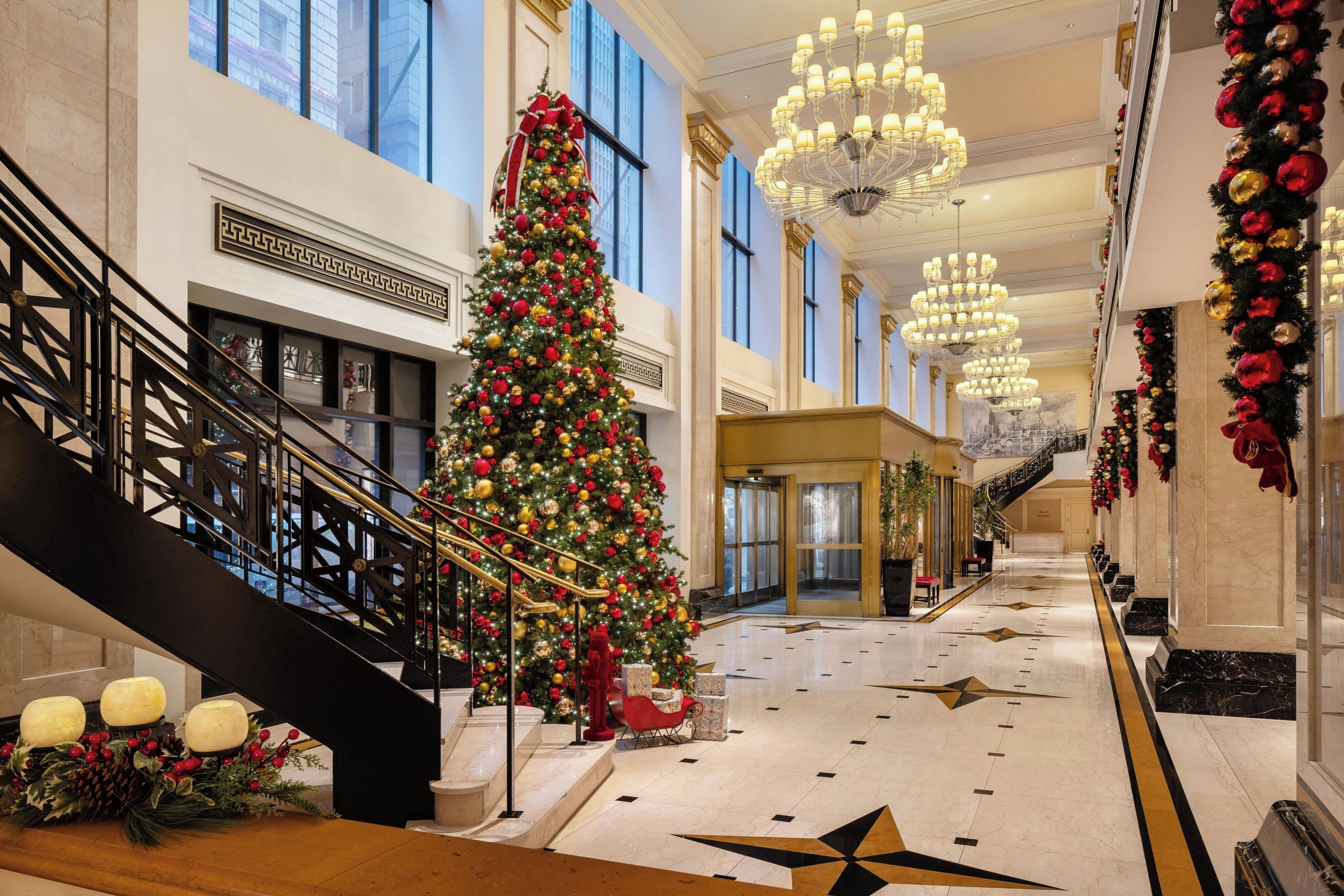A grand hotel lobby with a large Christmas tree, a grand staircase, and a star-patterned floor.