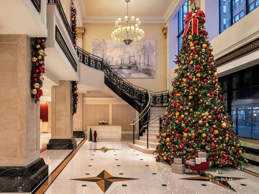 Un lobby imponente con un gran árbol de Navidad, pisos de mármol y una escalera.