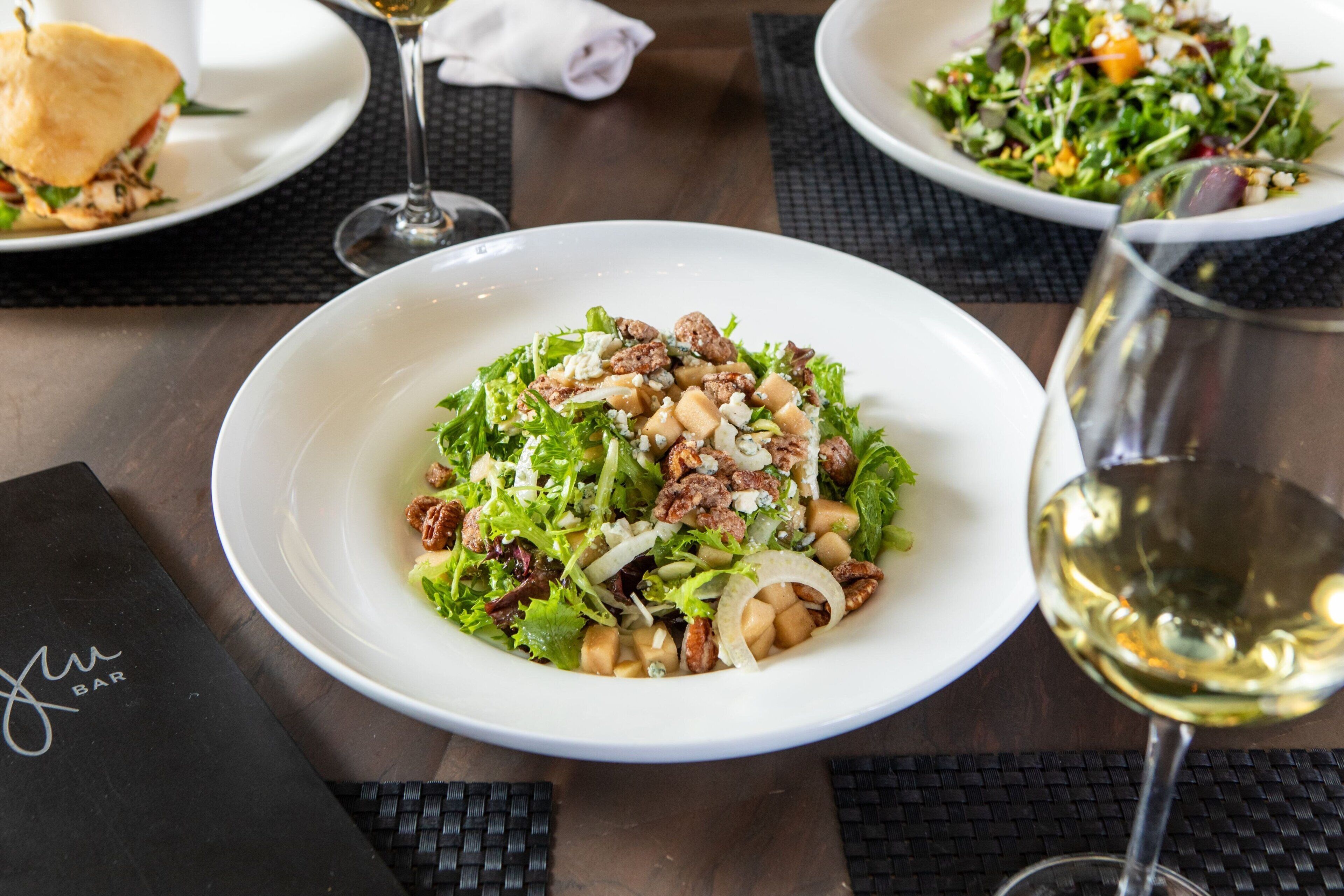 A table with a salad, a sandwich, and a glass of white wine.