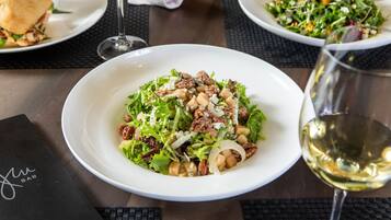 A table with a salad, a sandwich, and a glass of white wine.
