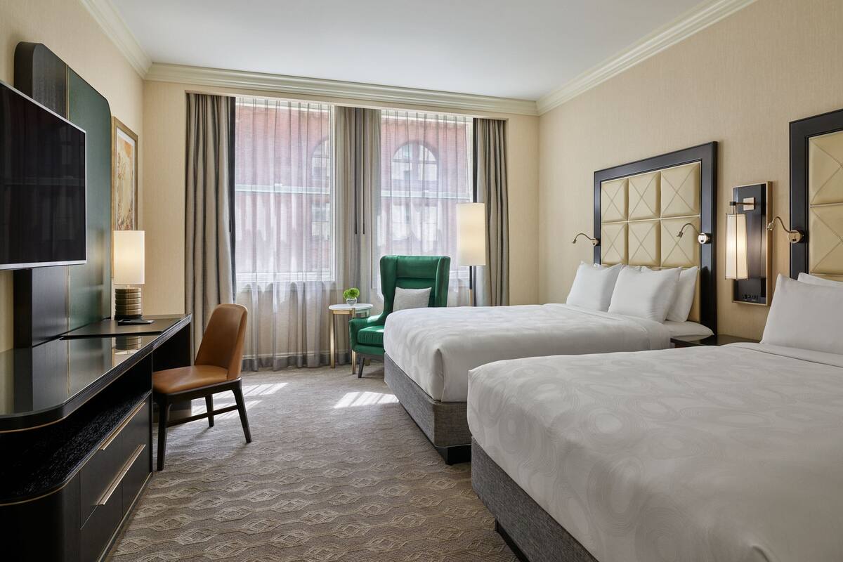 Une chambre d’hôtel avec deux lits, un bureau, une télévision et une chaise.