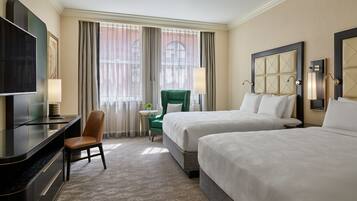 A hotel room with two beds, a desk with a chair, a television, and a window with curtains.