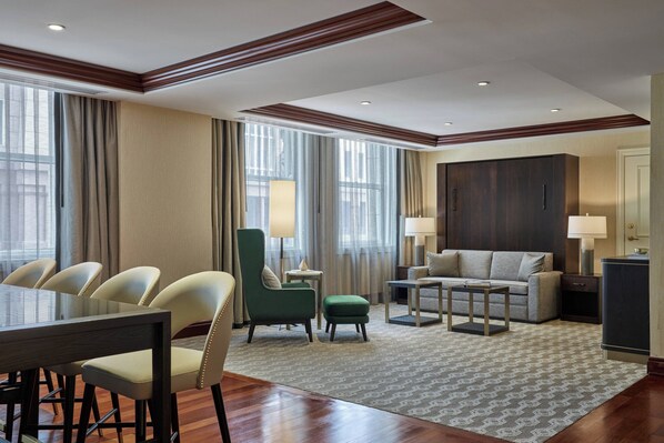 Habitación de hotel con comedor, sofá, sillón verde y un espejo grande.