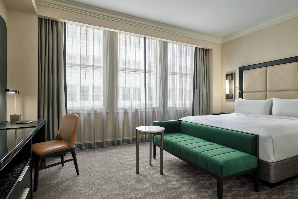 Une chambre d’hôtel avec un lit, un canapé vert, une chaise, une petite table et un bureau.