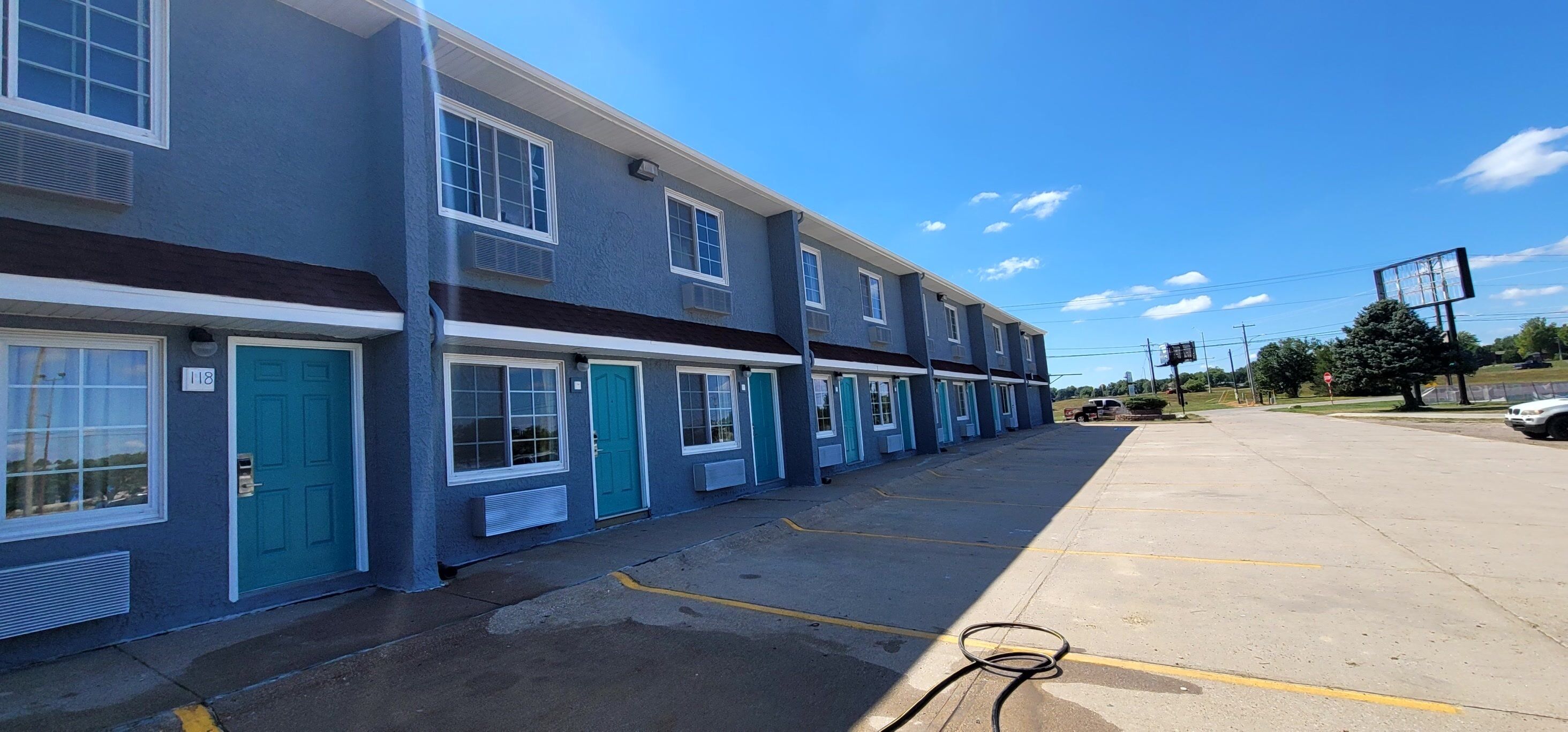 A row of blue and white buildings with numbered doors, a parking lot, and a clear sky.