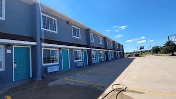 A row of blue and white buildings with numbered doors, a parking lot, and a clear sky.