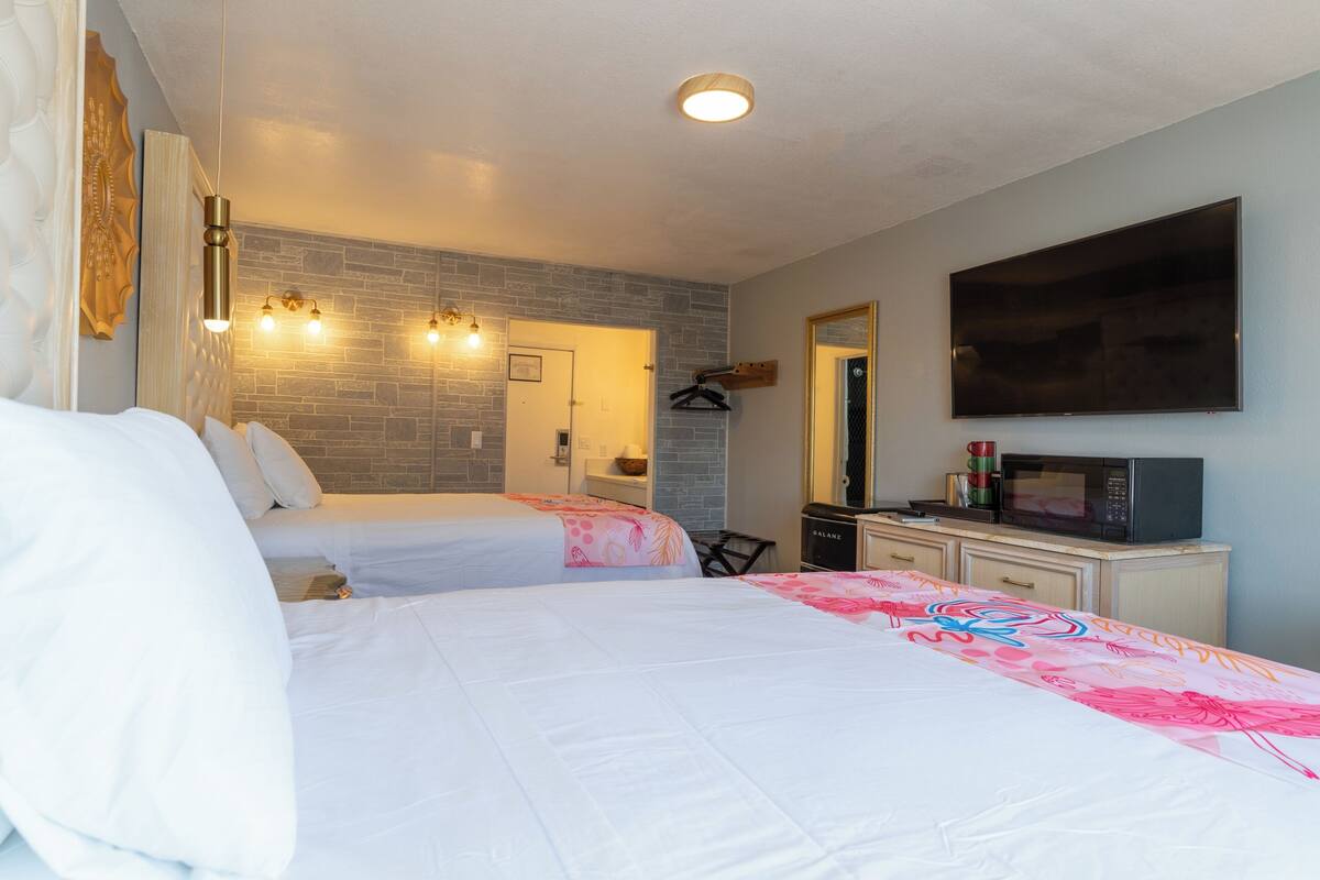 A hotel room with two beds, a flat-screen TV, a microwave, and a small desk.