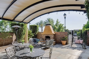 An outdoor patio with a brick oven, tables, chairs, and a covered seating area.