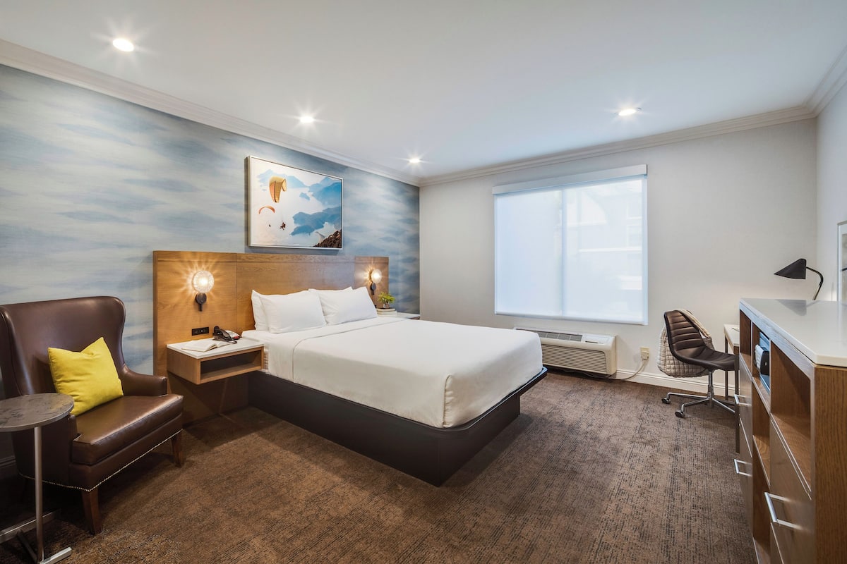 Ein Hotelzimmer mit Bett, Schreibtisch, Stuhl, kleinem Tisch und Fenster.