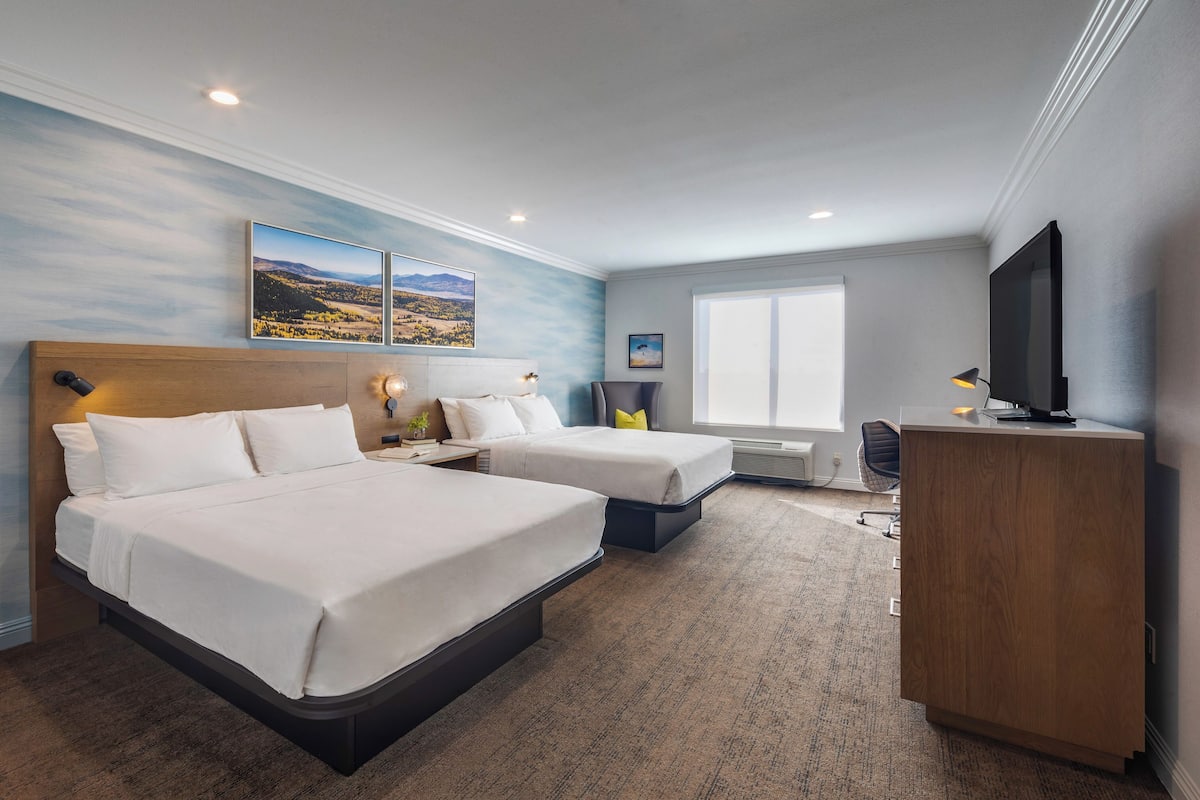Ein Hotelzimmer mit zwei Betten, einem Schreibtisch, einem Fernseher und Bildern an den Wänden.