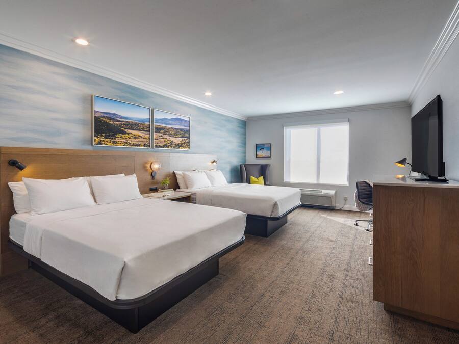 A hotel room with two beds, a desk, a television, and artwork on the walls.