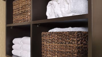 A bathroom with a black countertop, a sink, and shelves holding white towels and wicker baskets.