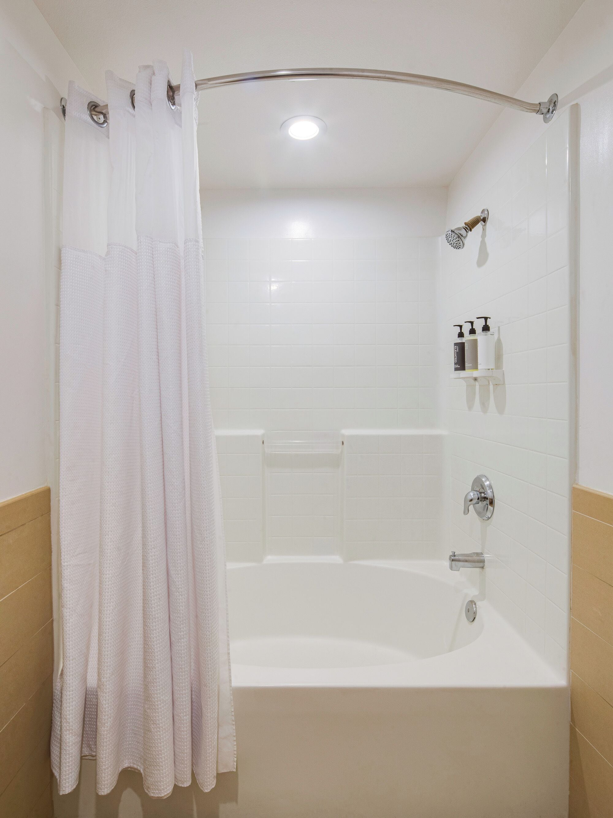Baño con bañera, ducha y repisa con artículos de aseo.