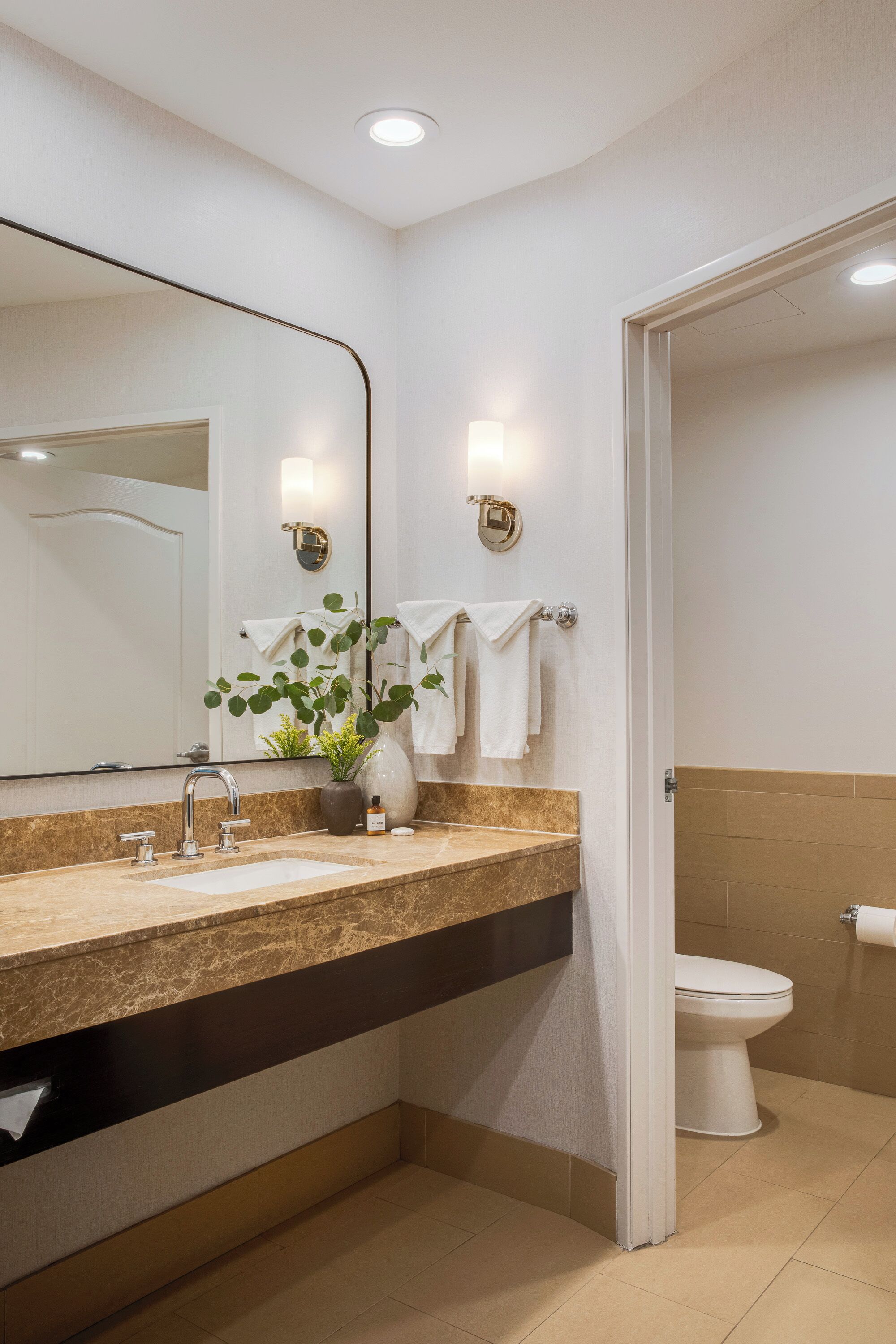 Een moderne badkamer met een marmeren aanrecht, een wastafel, een spiegel en een toilet.