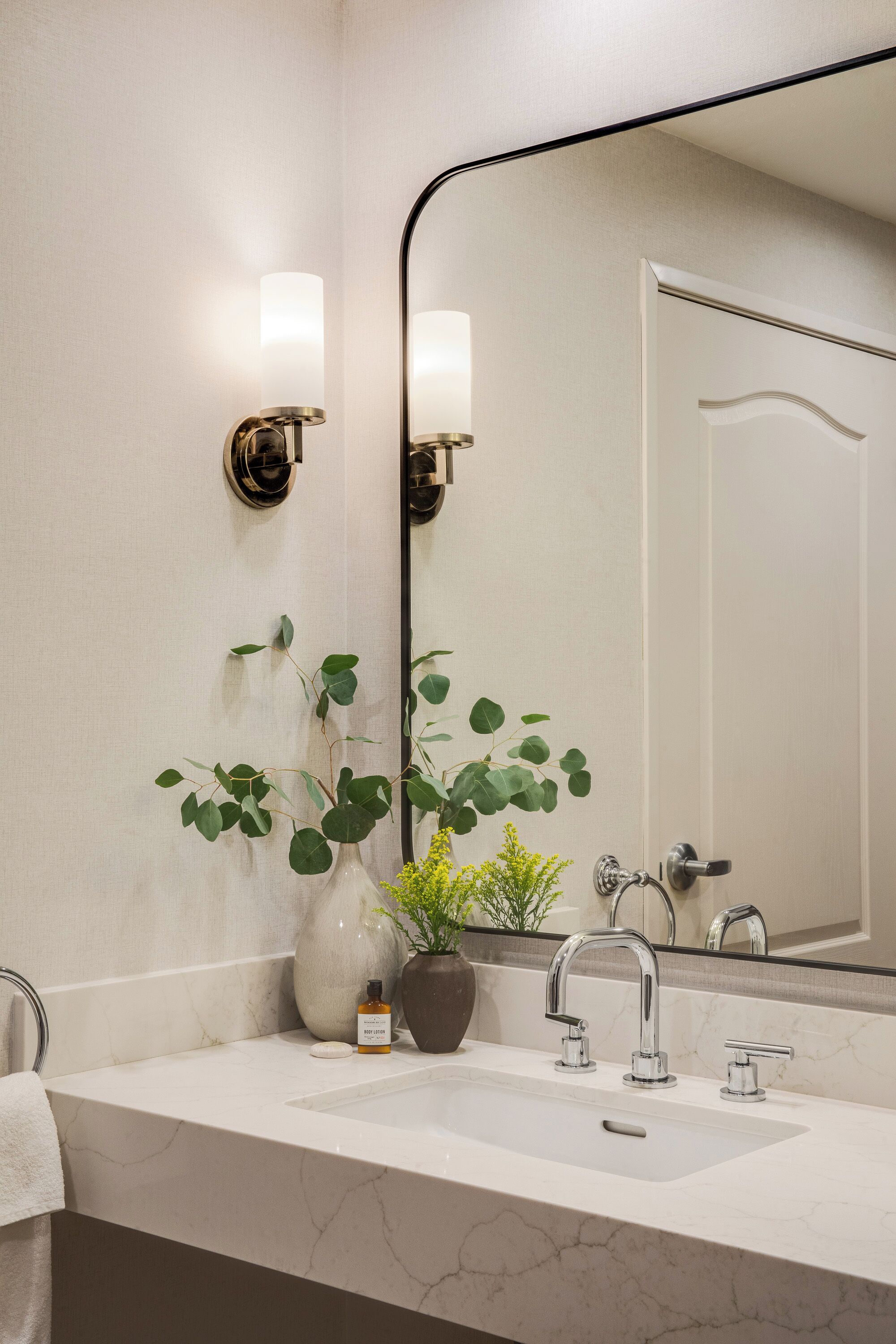 Une salle de bain avec un lavabo en marbre blanc, deux appliques murales, un grand miroir et une plante en pot.
