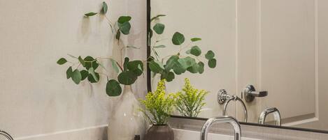 Une salle de bain avec un lavabo en marbre blanc, deux appliques murales, un grand miroir et une plante en pot.