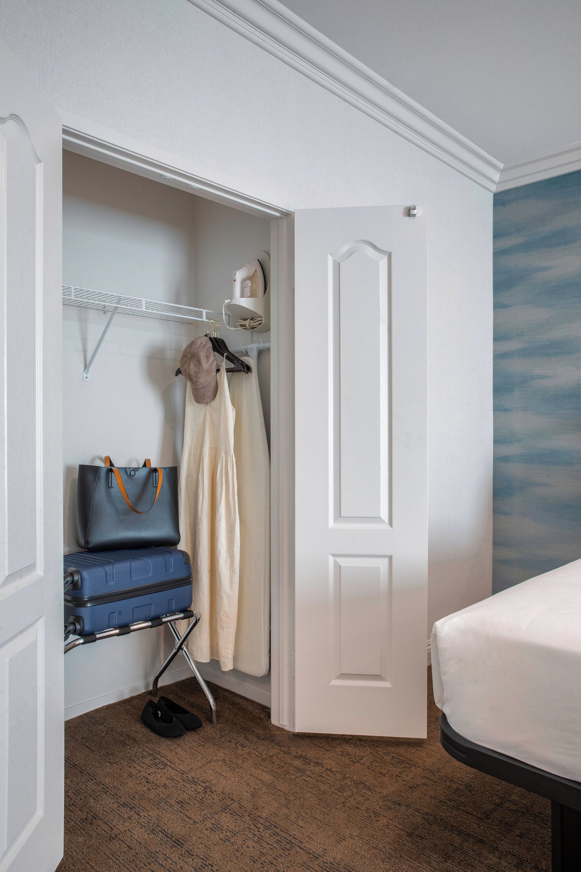 A hotel room with a bed, a suitcase, a handbag, and a hanging garment rack.