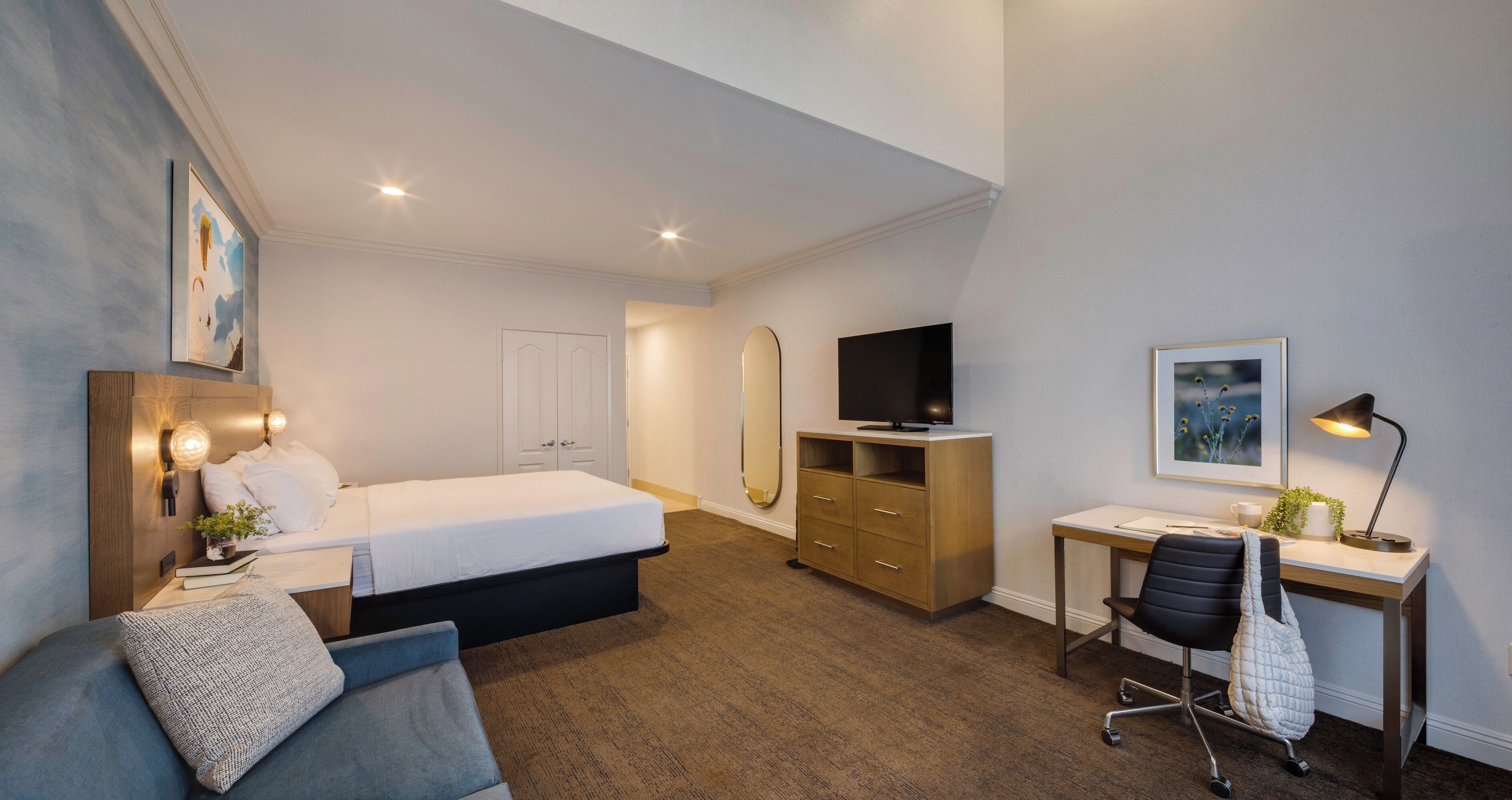Et moderne hotelværelse med seng, skrivebord, stol og fjernsyn.