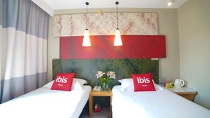 Habitación de hotel con dos camas, una mesita de noche con un teléfono, un florero con flores y una cafetera.