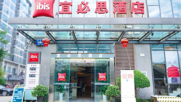 Exterior del hotel ibis con señalización clara, fachada moderna de vidrio y un adorno de farolillo rojo.